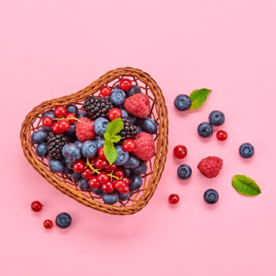 Blueberry, raspberry, blackberry, redcurrant in heart basket. Fresh blueberry, berries mix on pink. Red raspberry, mint creative composition. Colorful concept, top view.